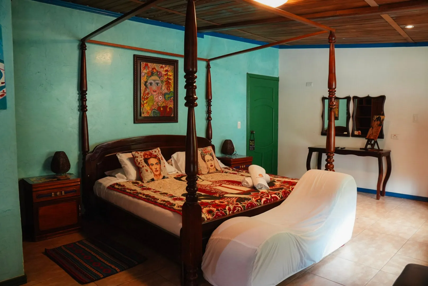 Cama con dosel de madera de la habitación Casa Azul, con paredes turquesa y cuadro sobre la cabecera