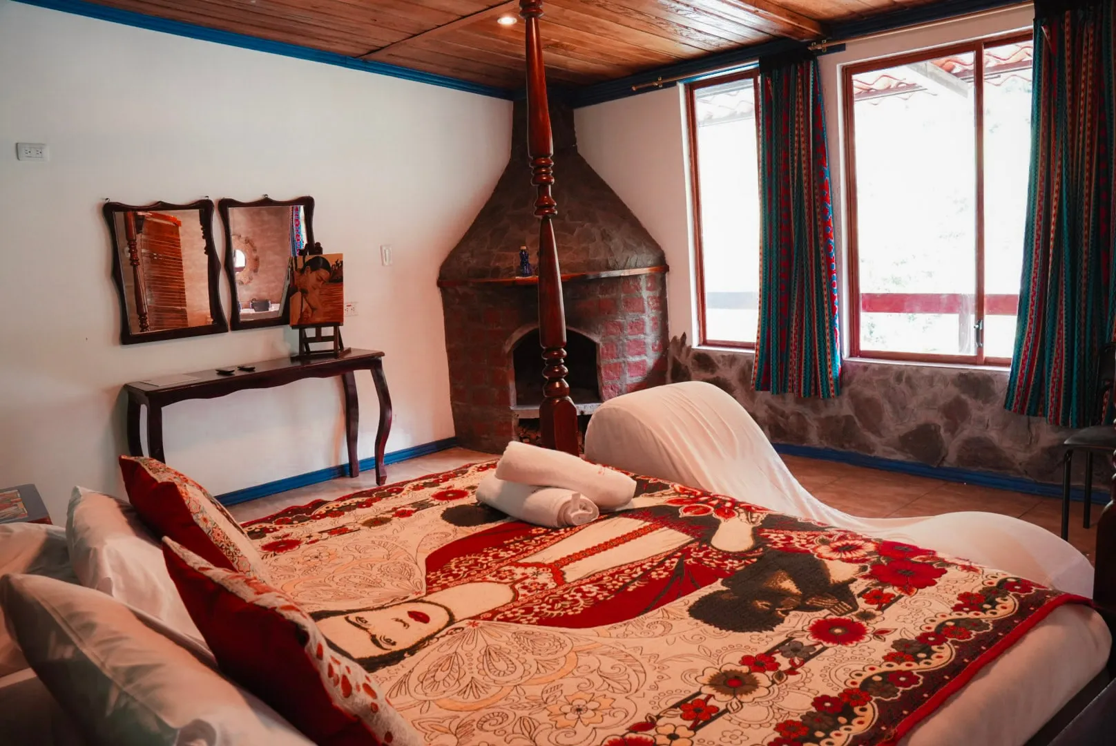 Chimenea de ladrillo y ventanas de la habitación Casa Azul, con la cama con dosel en primer plano